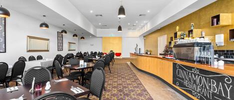 Un comedor de hotel con mesas, sillas, una recepción y una máquina de café.