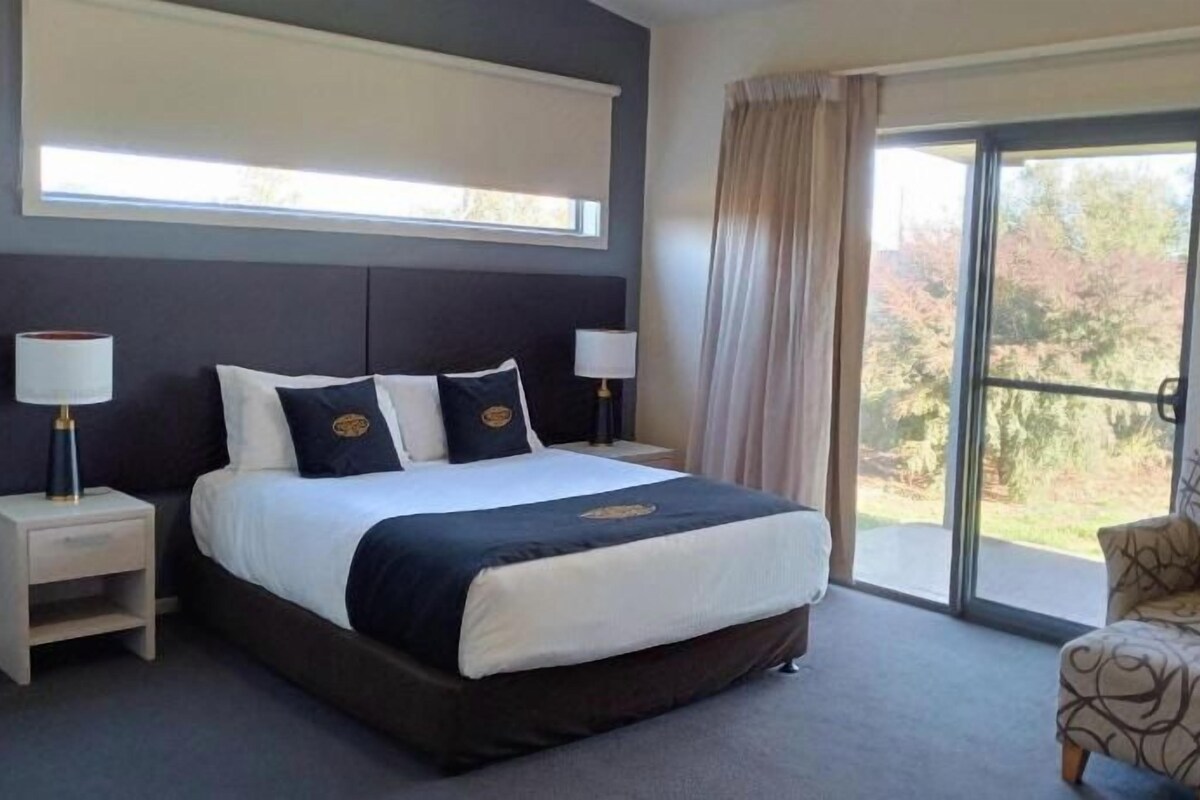A hotel room with a large bed, a chair, a nightstand, and a window with curtains.