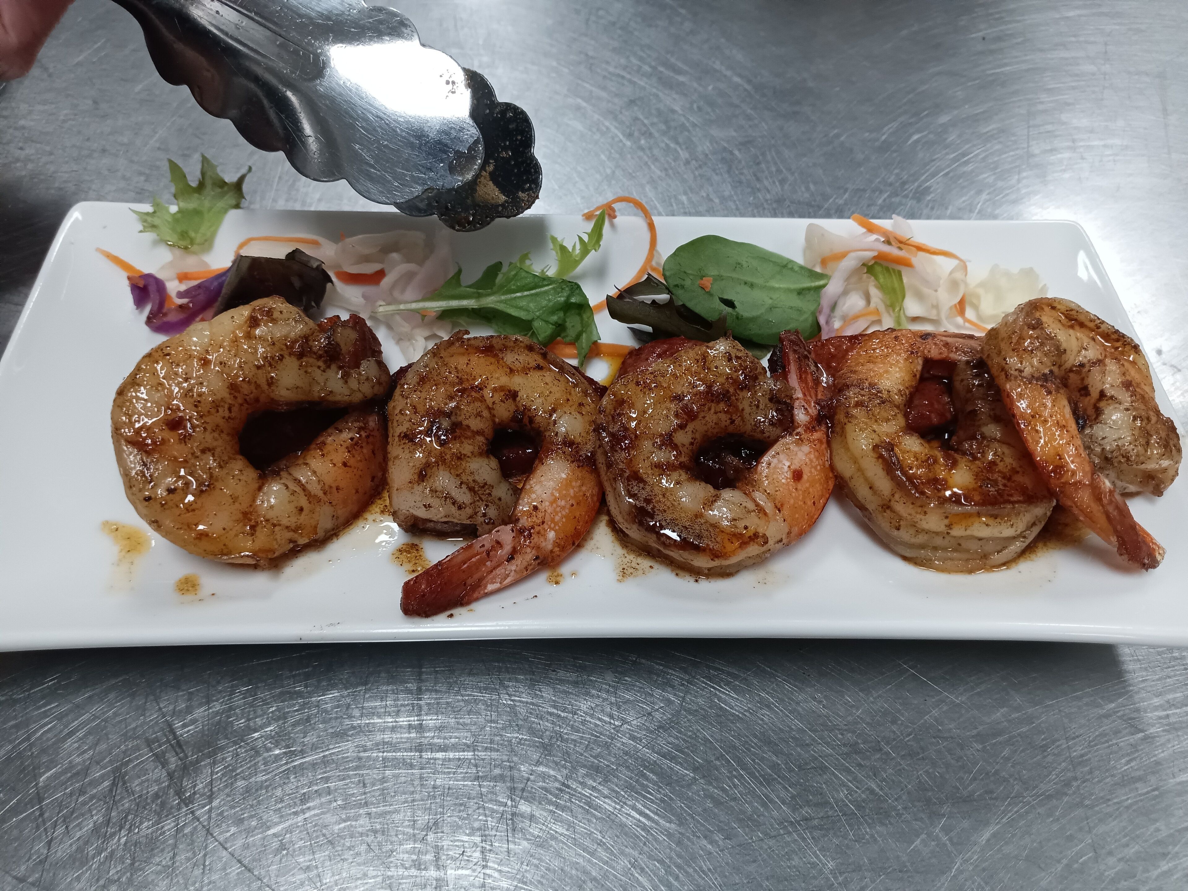 A plate of cooked shrimp with a garnish of greens and shredded carrots.