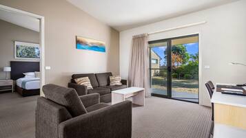 Ein modernes Hotelzimmer mit einer Couch, einem kleinen Tisch, einem Schreibtisch, einem Bett und einer großen Schiebeglas-Tür, die auf einen Balkon führt.