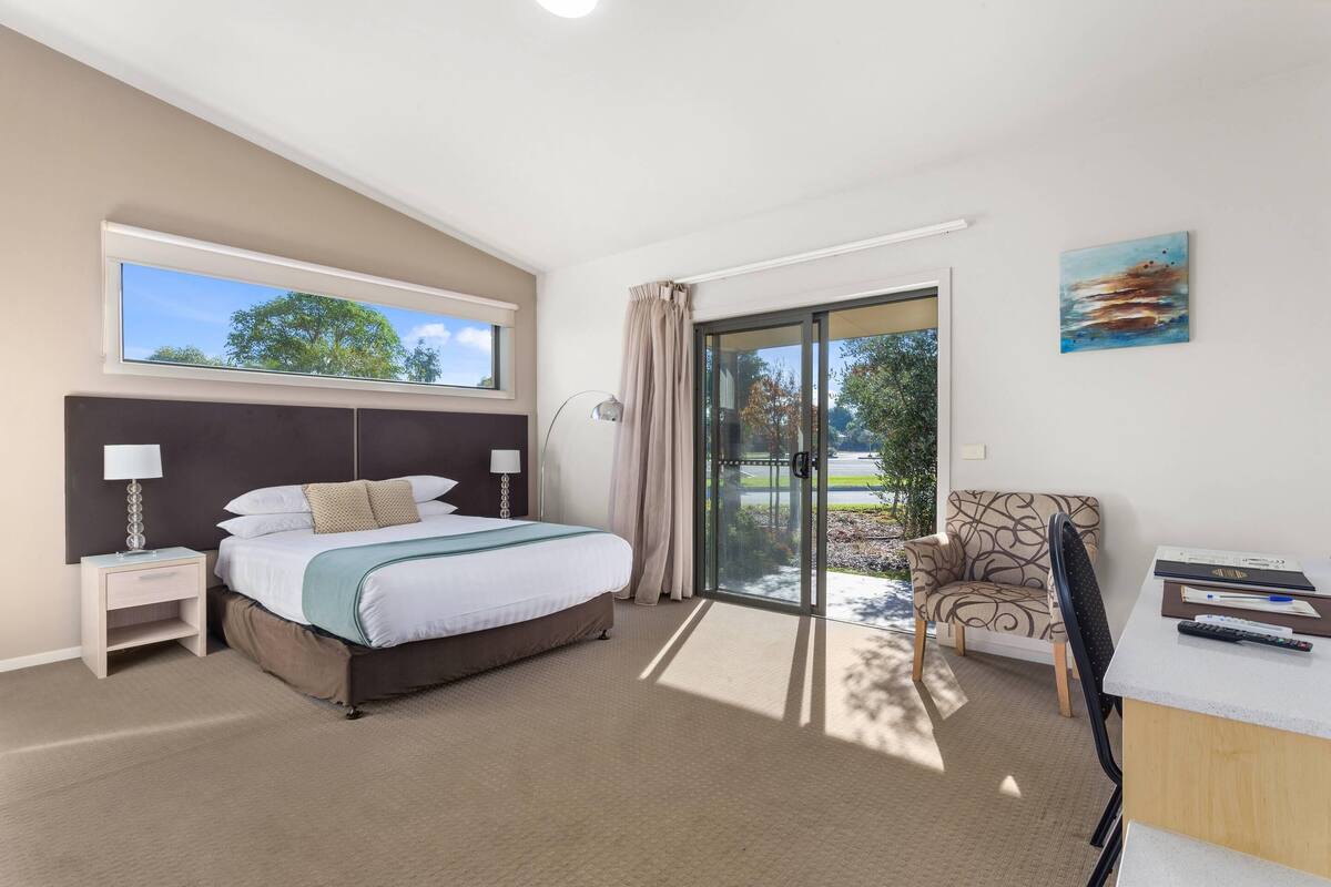 A bedroom with a bed, a desk, a chair, a window, and a door leading to a balcony.