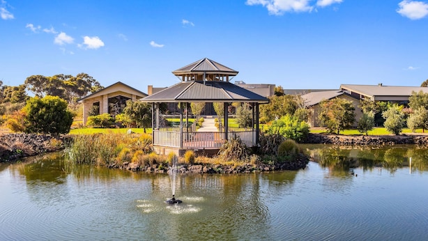 A gazebo with a pond in front, surrounded by trees and a building in the background. - Quality Hotel Point Cook (Point Cook)