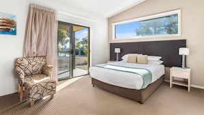 A bedroom with a bed, a chair, a nightstand, a window, and a door leading to an outdoor area. - Quality Hotel Point Cook (Point Cook)