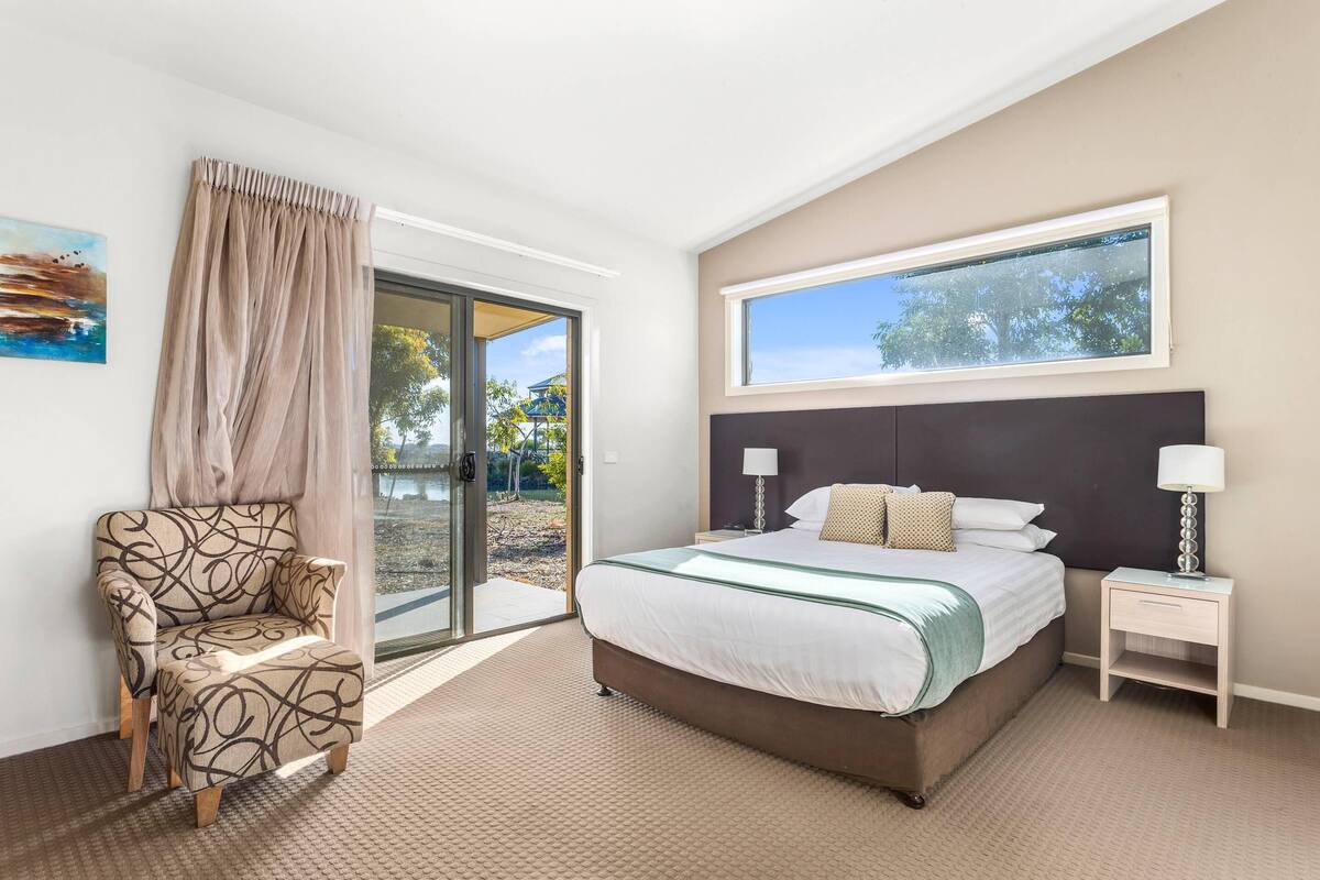 A bedroom with a bed, a chair, a nightstand, a window, and a door leading to an outdoor area.