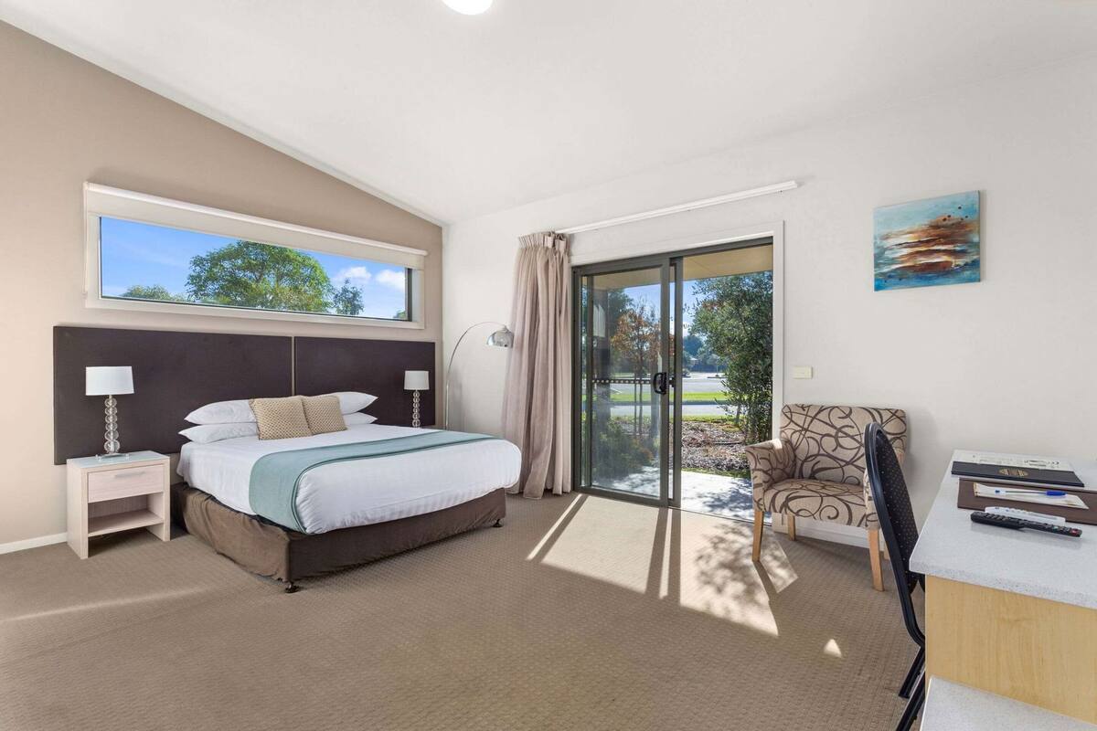 A bedroom with a bed, a desk, a chair, a window, and a door leading to a balcony.
