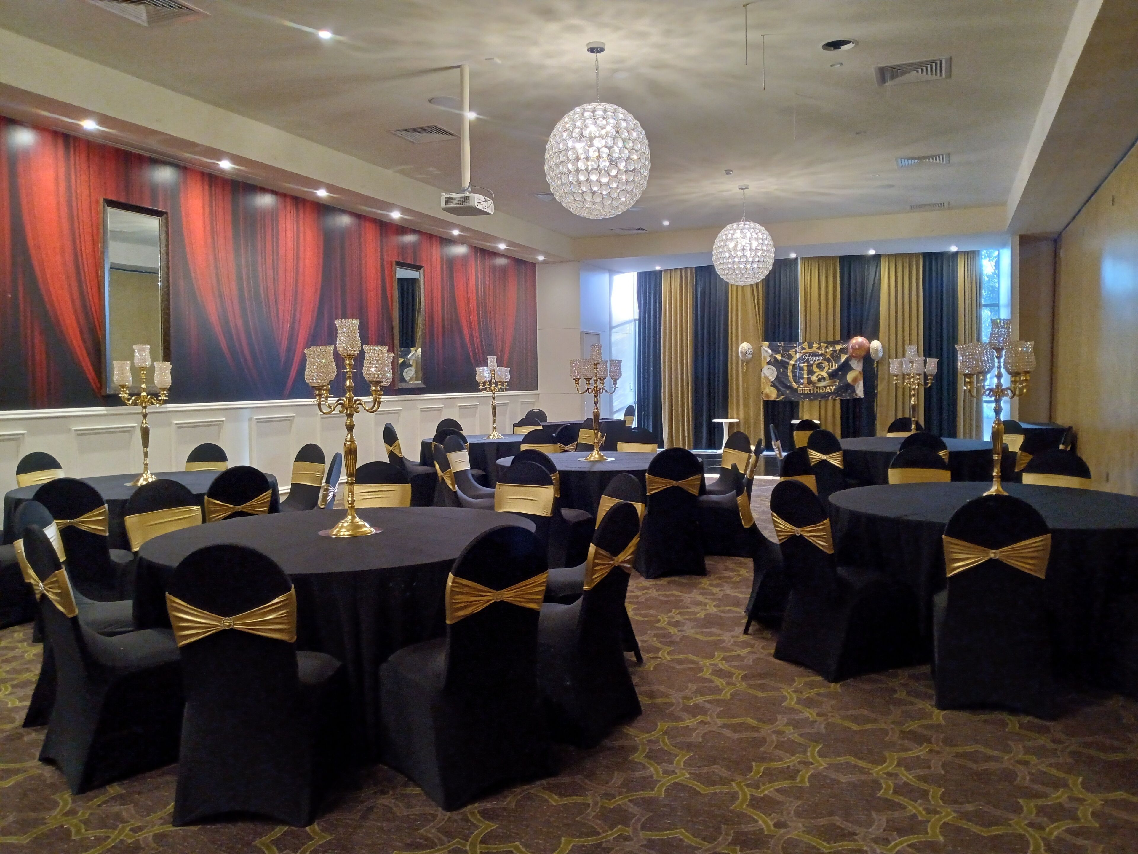 Une salle de banquet avec des tables rondes, des chaises noires ornées de rubans dorés et des lustres.