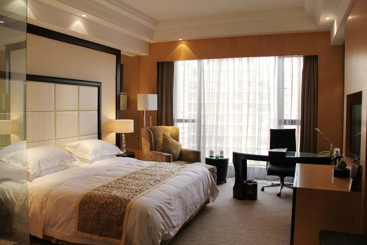 Quarto de hotel com uma cama grande, uma escrivaninha, uma cadeira e uma televisão.