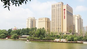 Un hotel de gran altura con varios pisos, un logotipo destacado en la fachada y una vista de una masa de agua con una lancha en primer plano.