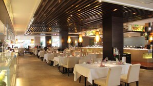 Un restaurante con varias mesas dispuestas para comer, con un diseño interior moderno que incluye paneles de madera e iluminación colgante.