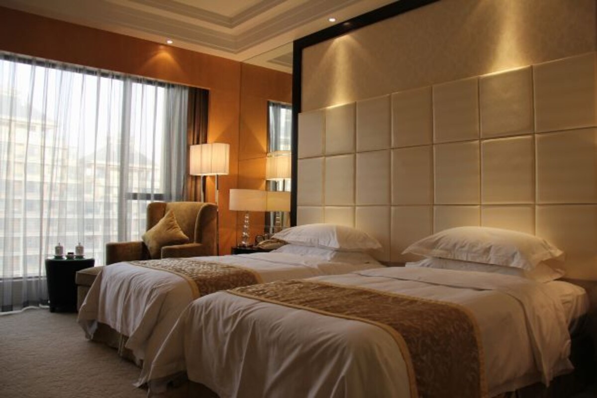 Habitación de hotel con dos camas, un ventanal con cortinas, una silla y una mesita de noche con lámpara.