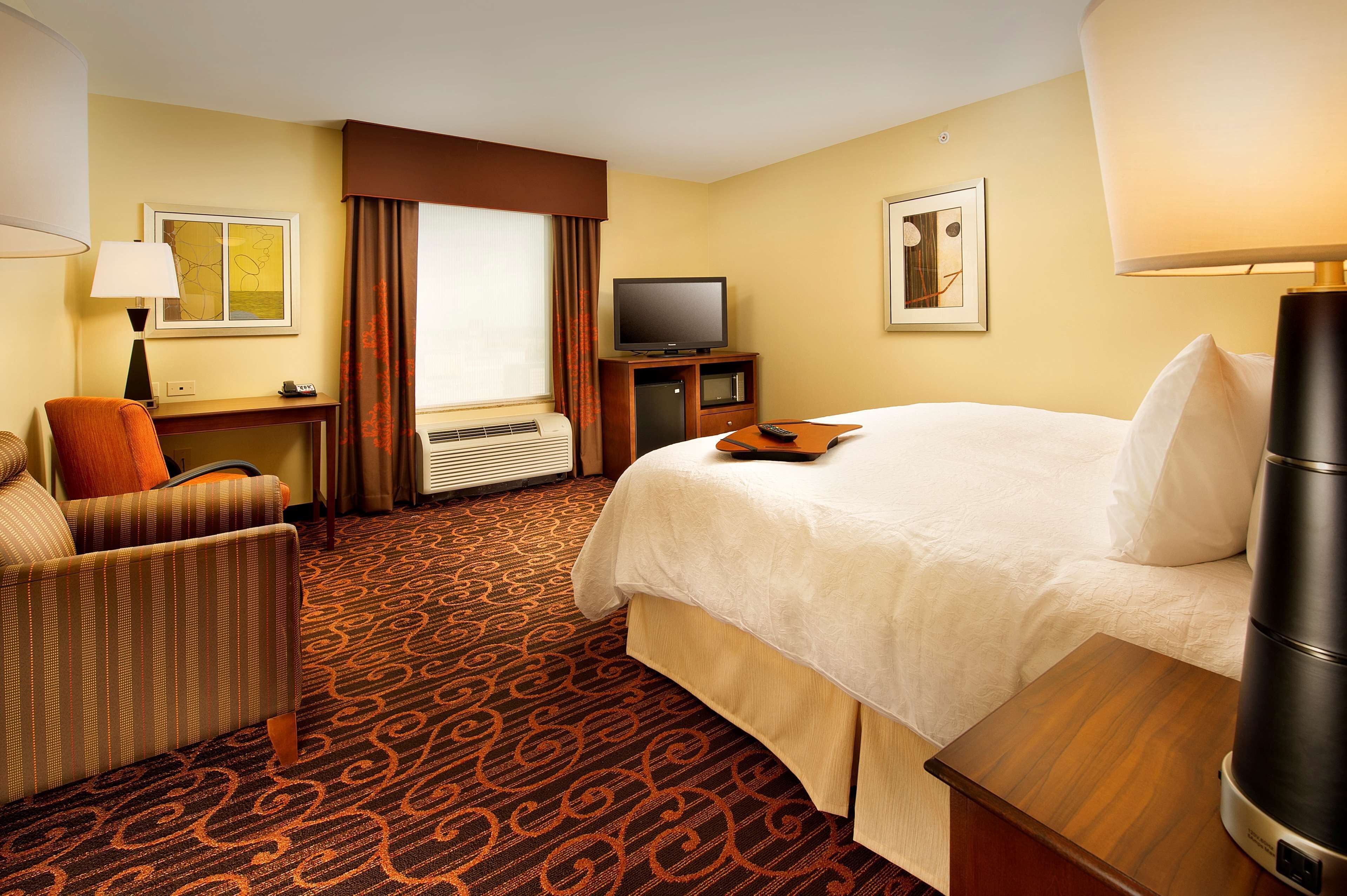 Ein Hotelzimmer mit einem großen Bett, einem Schreibtisch mit Fernseher, einem Sessel und einer Kaffeemaschine.