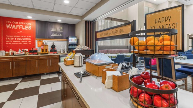 Un espacio para desayunar con estación de waffles, exhibición de frutas y zona de estar.