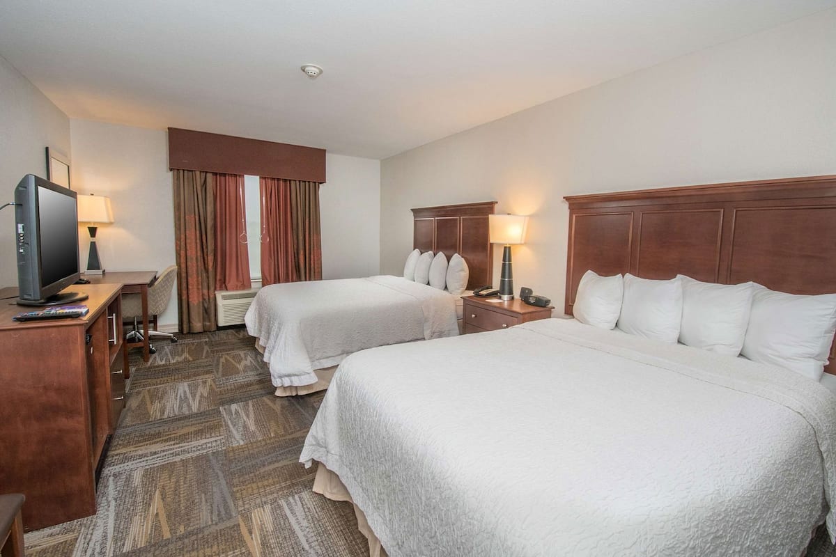 Habitación de hotel con dos camas, un escritorio, televisor, lámpara y teléfono.