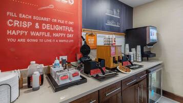 A waffle station with a red sign, a waffle maker, and various condiments.