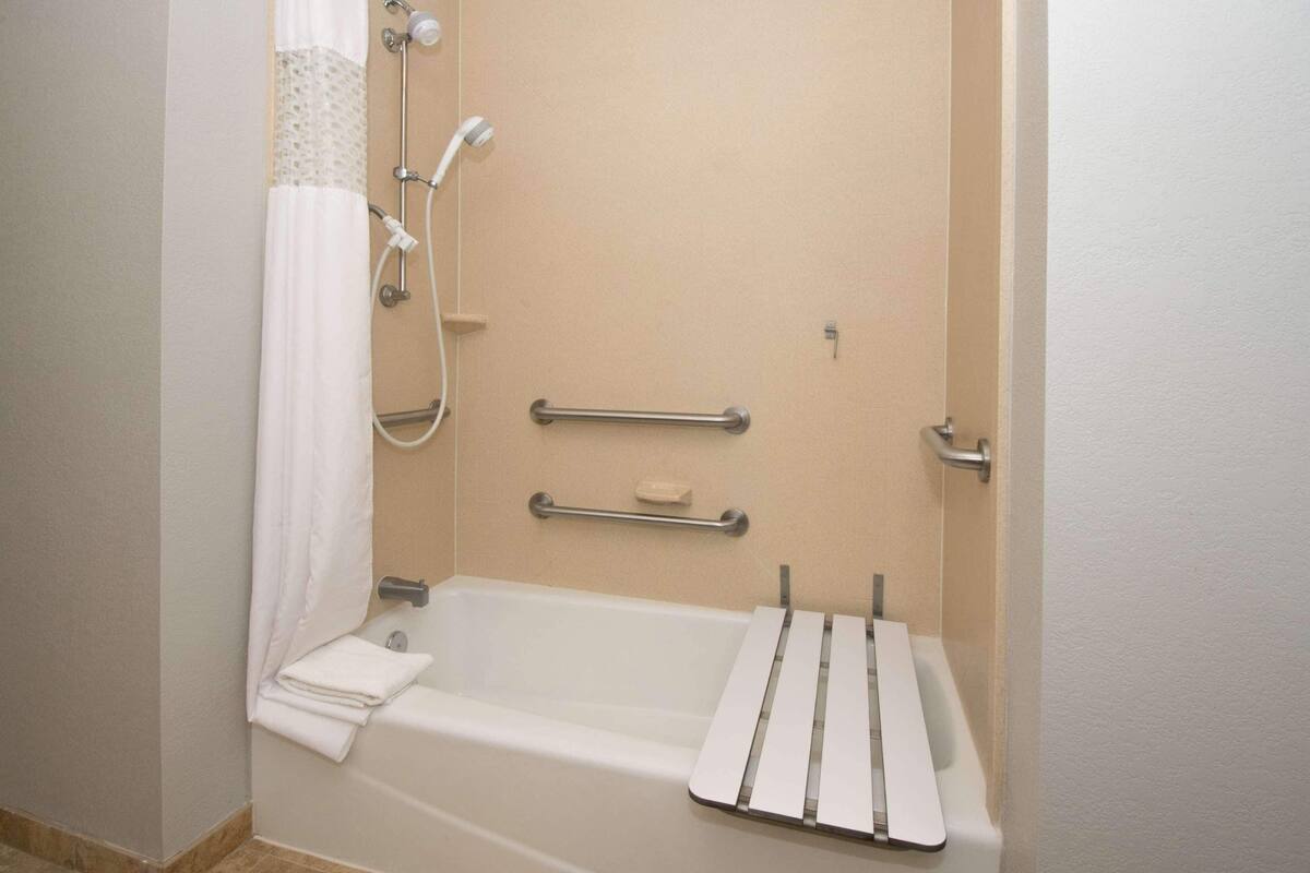 Un baño con bañera, barras de apoyo, toallero y cabezal de ducha.