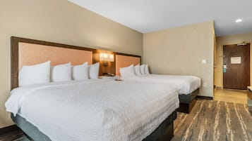 Ein Hotelzimmer mit zwei Betten, einem Kopfteil mit Lampenaufsatz, einer Holztür und einem Teppichboden.