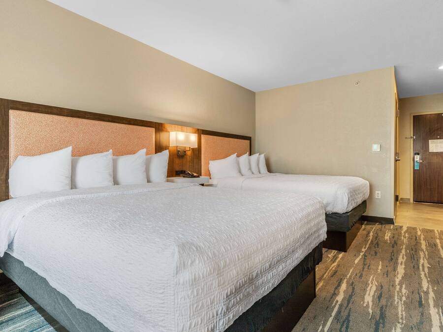 Ein Hotelzimmer mit zwei Betten, einem Kopfteil mit Lampenaufsatz, einer Holztür und einem Teppichboden.