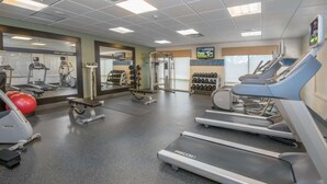 Un gimnasio con cintas de correr, máquinas de pesas y pesas libres.