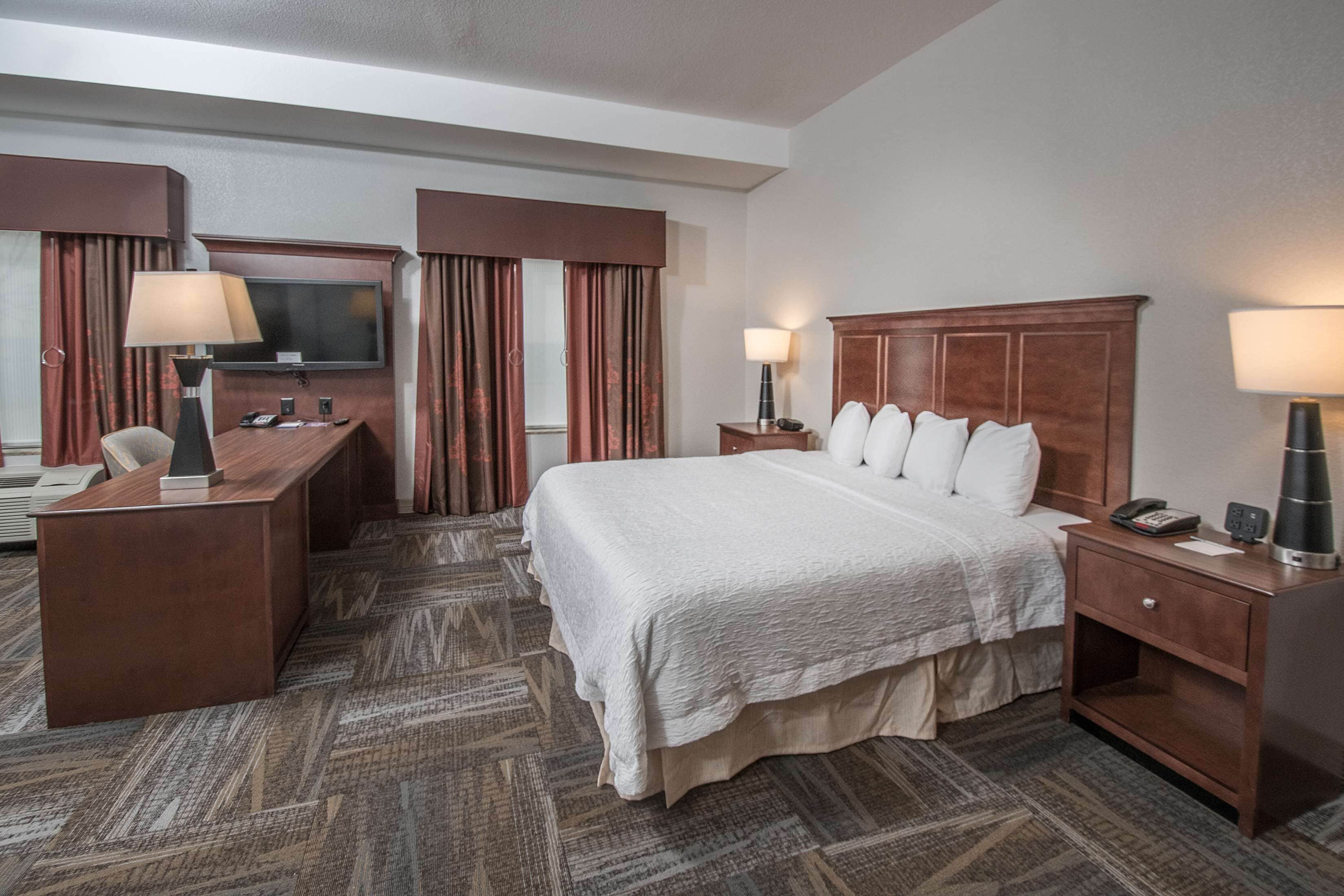 A hotel room with a large bed, a desk, a television, and a minibar.