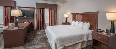 A hotel room with a large bed, a desk, a television, and a minibar.