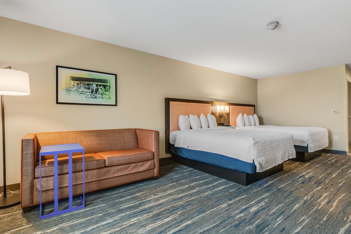 Habitación de hotel con cama doble, sofá, una mesita y un cuadro en la pared.