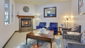Un salón con chimenea, sillones tapizados en azul, una mesa de centro y un reloj en la pared.