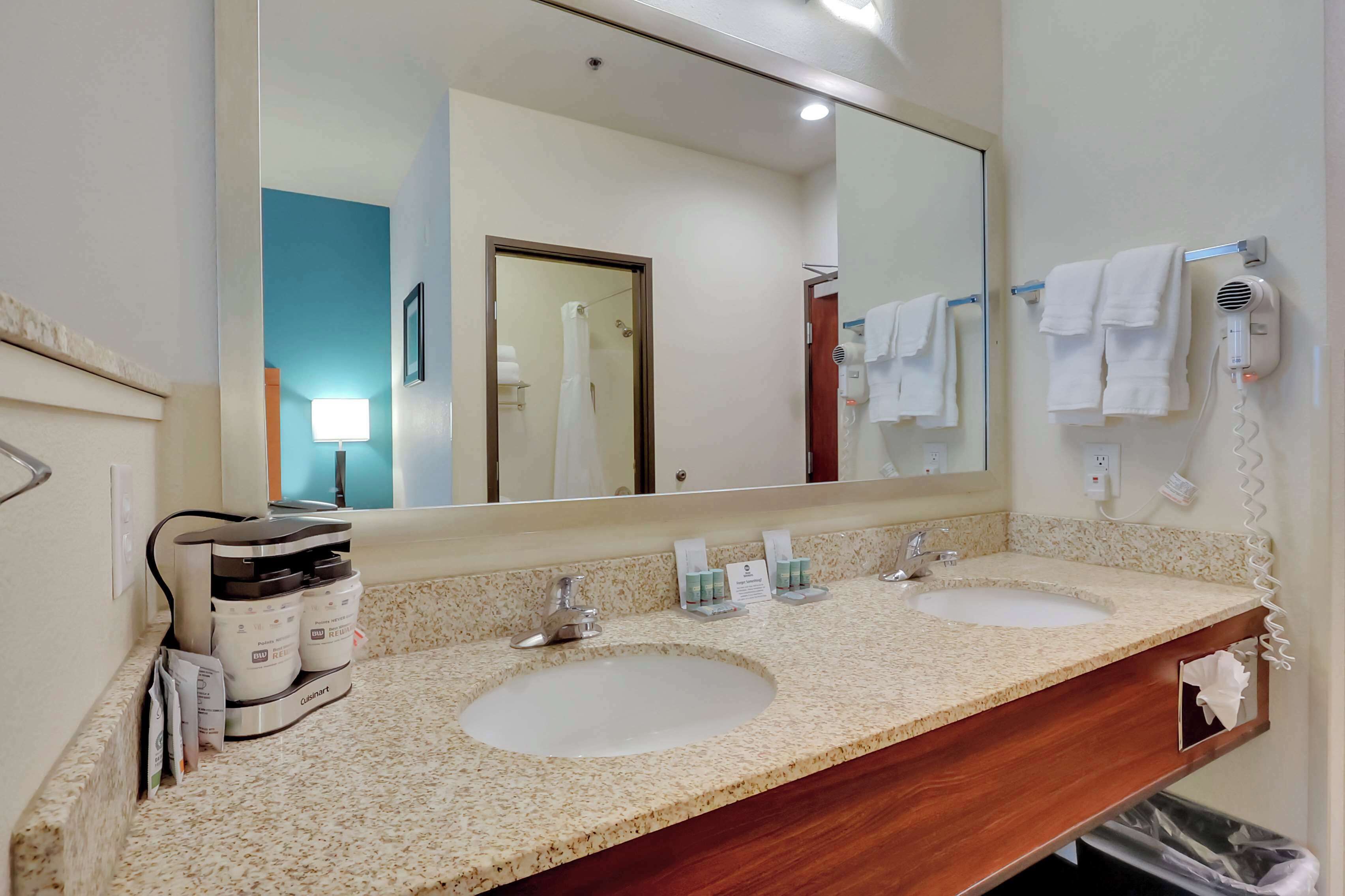 Une salle de bain avec deux lavabos, un grand miroir et un sèche-cheveux fixé au mur.