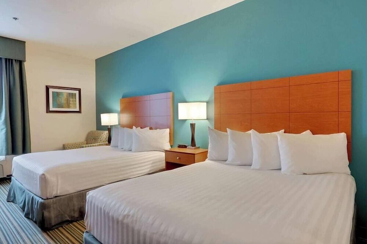 A hotel room with two beds, a headboard, bedside lamps, a nightstand, a framed picture on the wall, and a window with curtains.