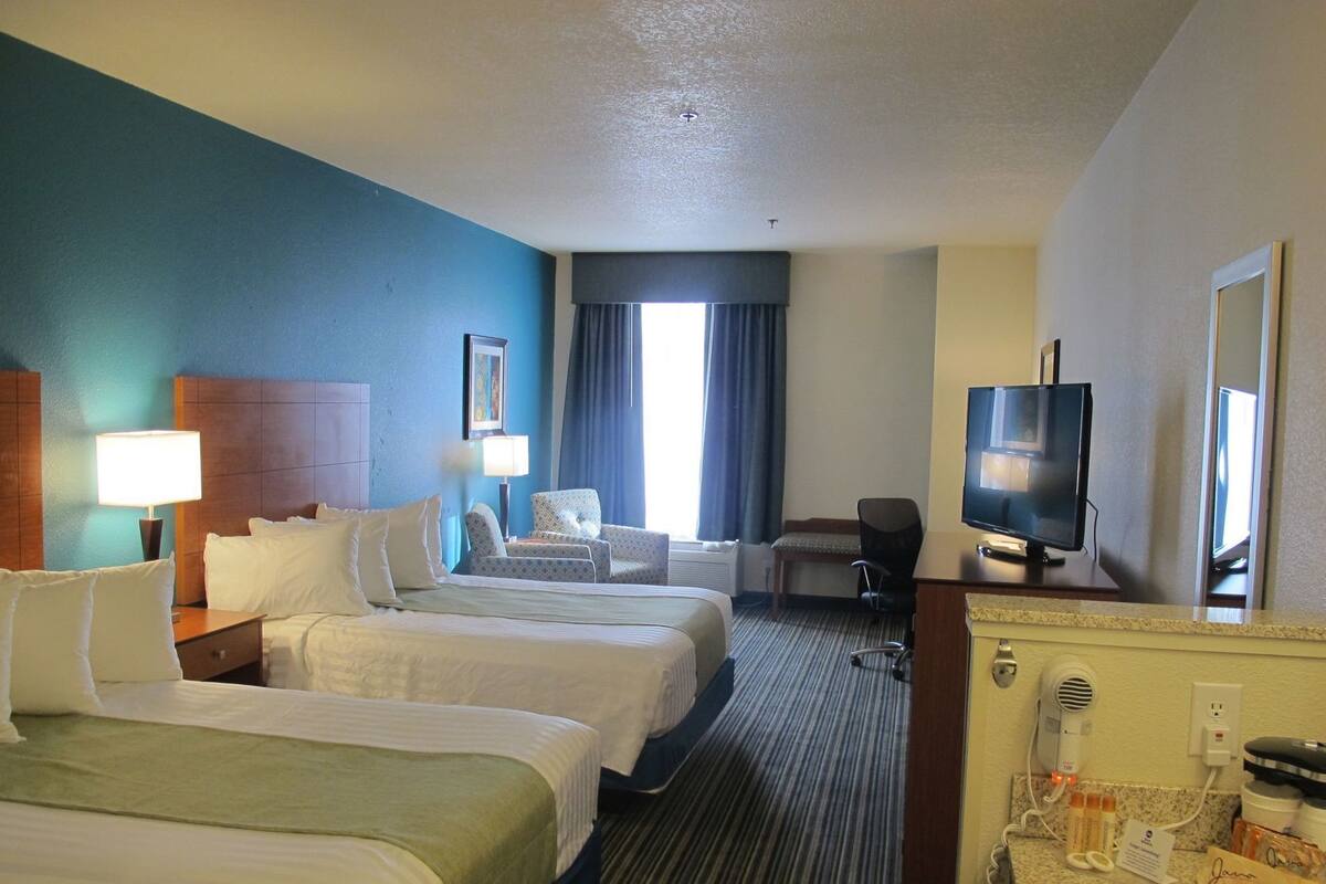 A hotel room with two beds, a desk with a TV, a chair, and a bathroom with a mirror and toiletries.