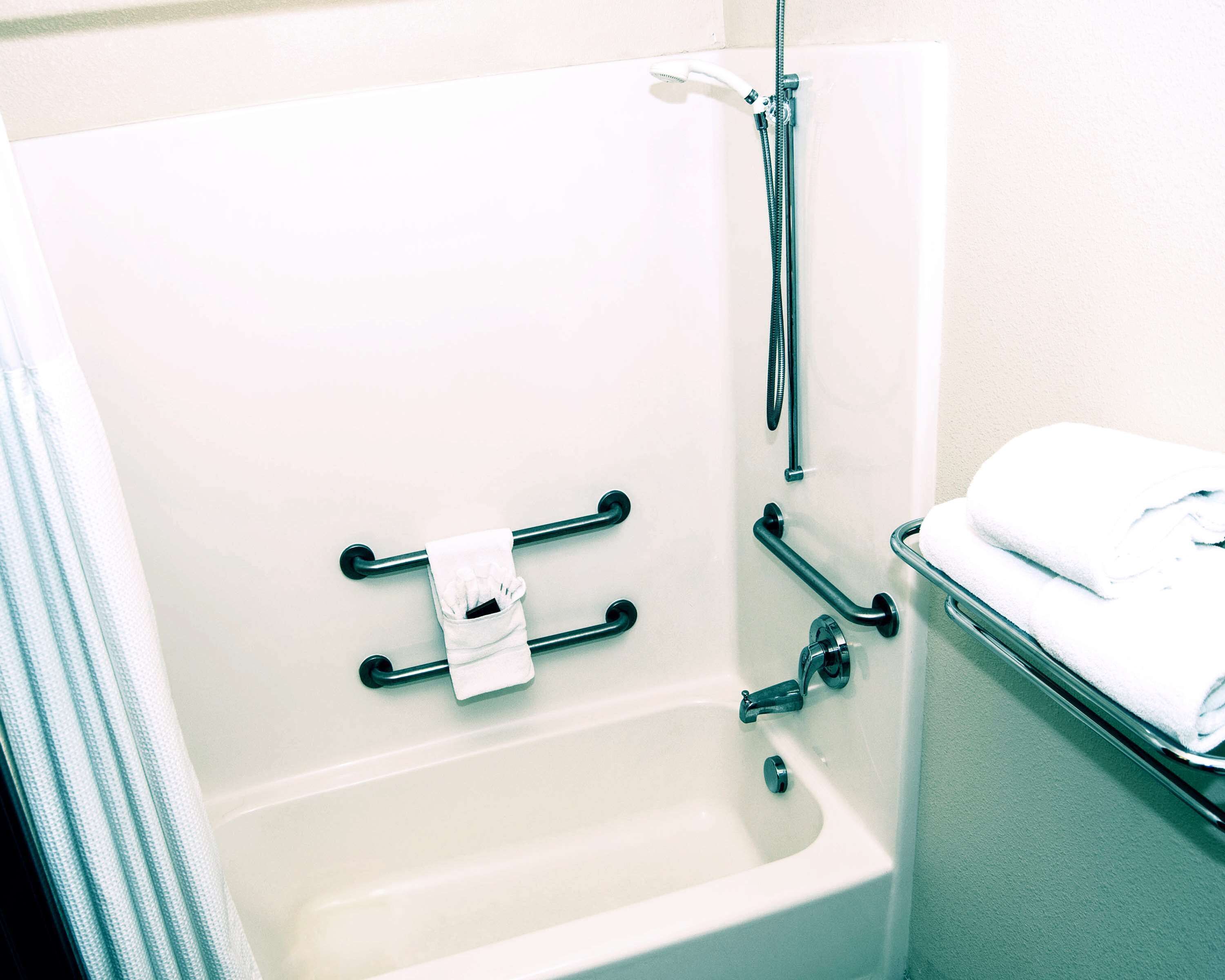 A bathtub with grab bars, a showerhead, and a towel rack.