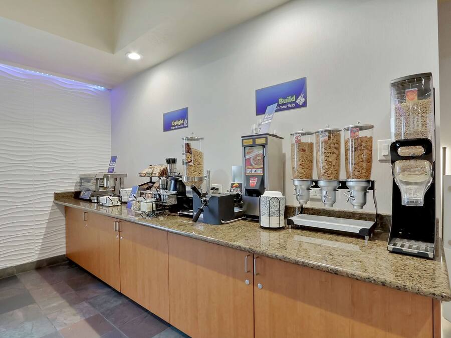 Un área de desayuno autoservicio con varios dispensadores de alimentos, una máquina de café y una balanza para pesar comida.