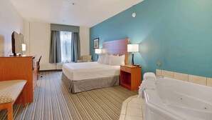 Habitación de hotel con cama, escritorio, silla, lámpara de escritorio, mesita de noche, lámpara, baño con bañera y ventana con cortinas.
