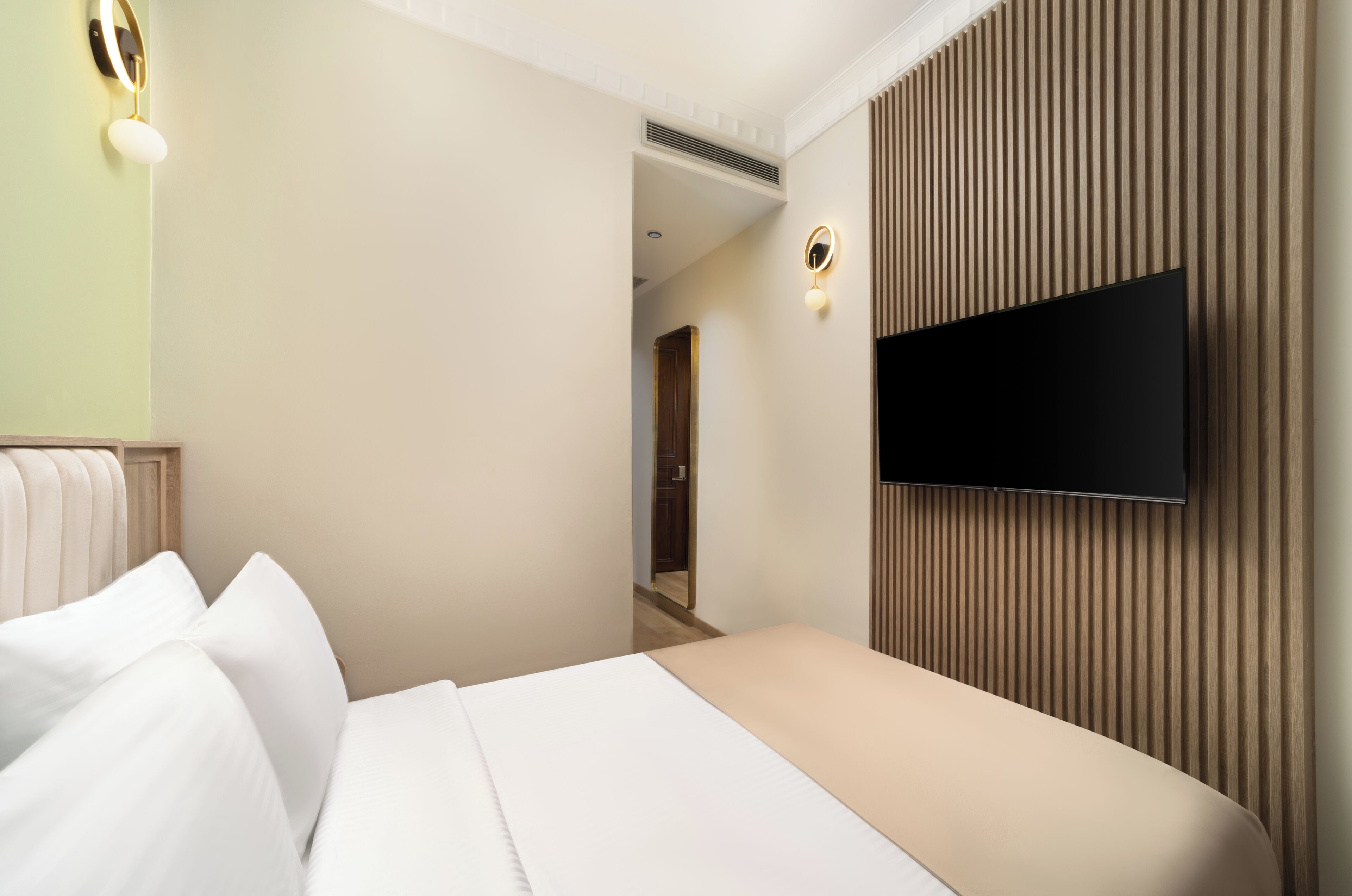 A hotel room with a bed, a TV mounted on the wall, and a hallway leading to another room.