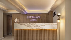 A reception desk with a marble top and wooden paneling, a neon sign reading "Atik Palace Hotel", and a floor lamp on the right. - Atik Palace Hotel (Istanbul)