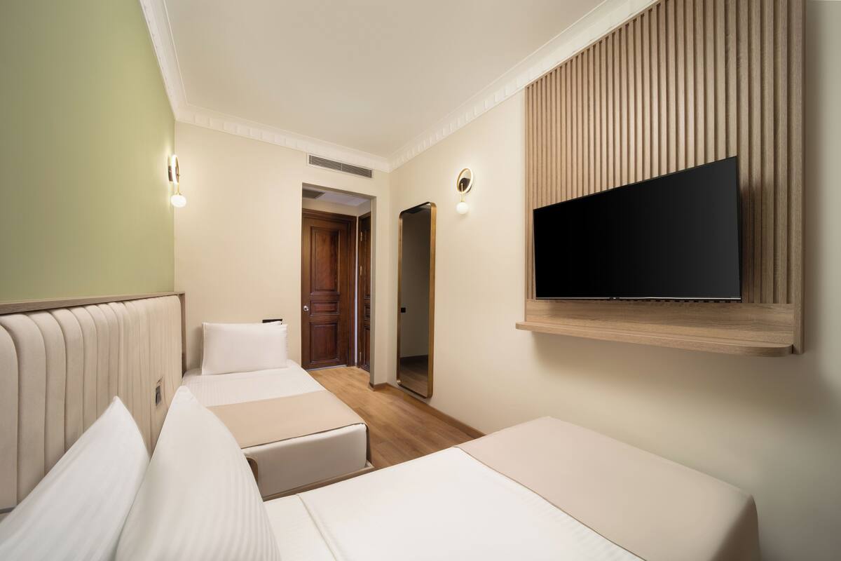 A hotel room with a bed, a television mounted on the wall, and a door leading to another room.
