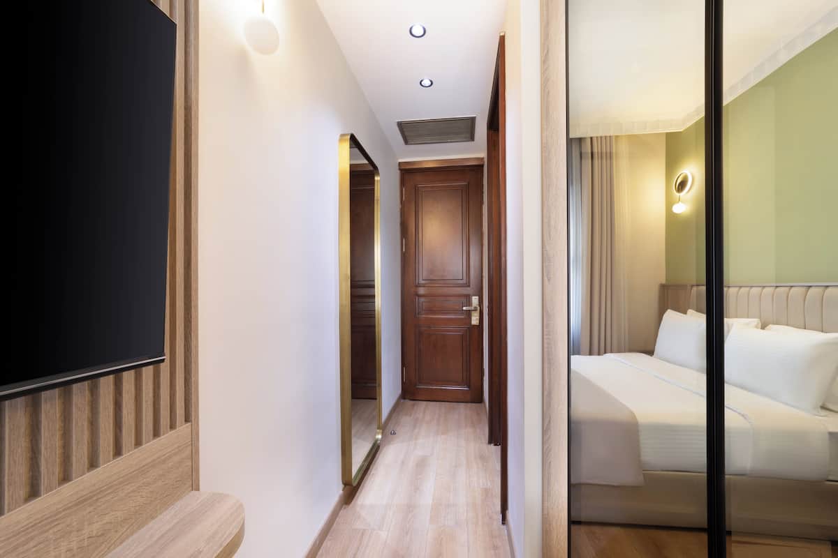 A hotel hallway with a wooden bench, a mirror, a door, and a bed with white bedding.