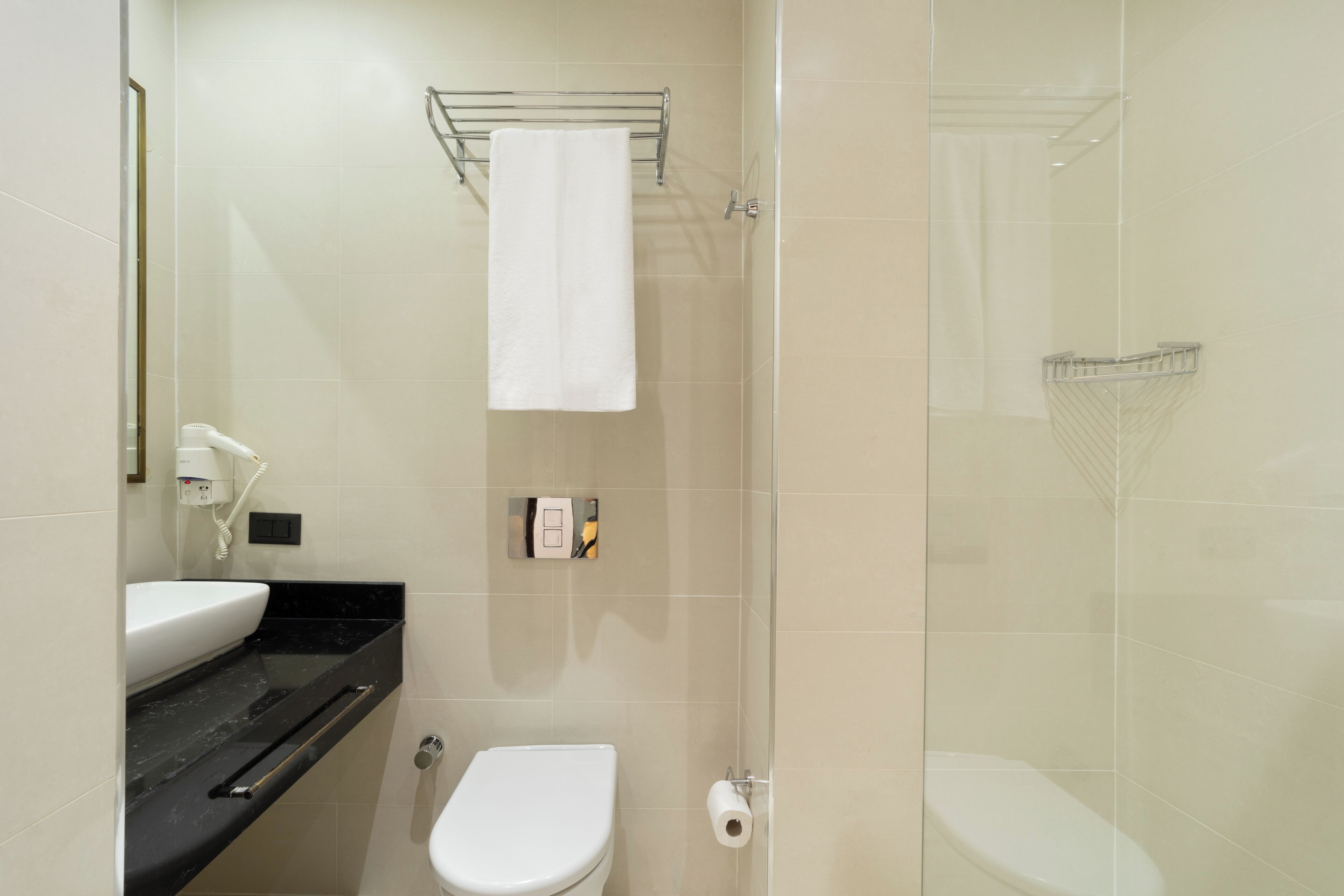 Un baño moderno con inodoro blanco, lavamanos con encimera negra, toallero y cabina de ducha de vidrio.