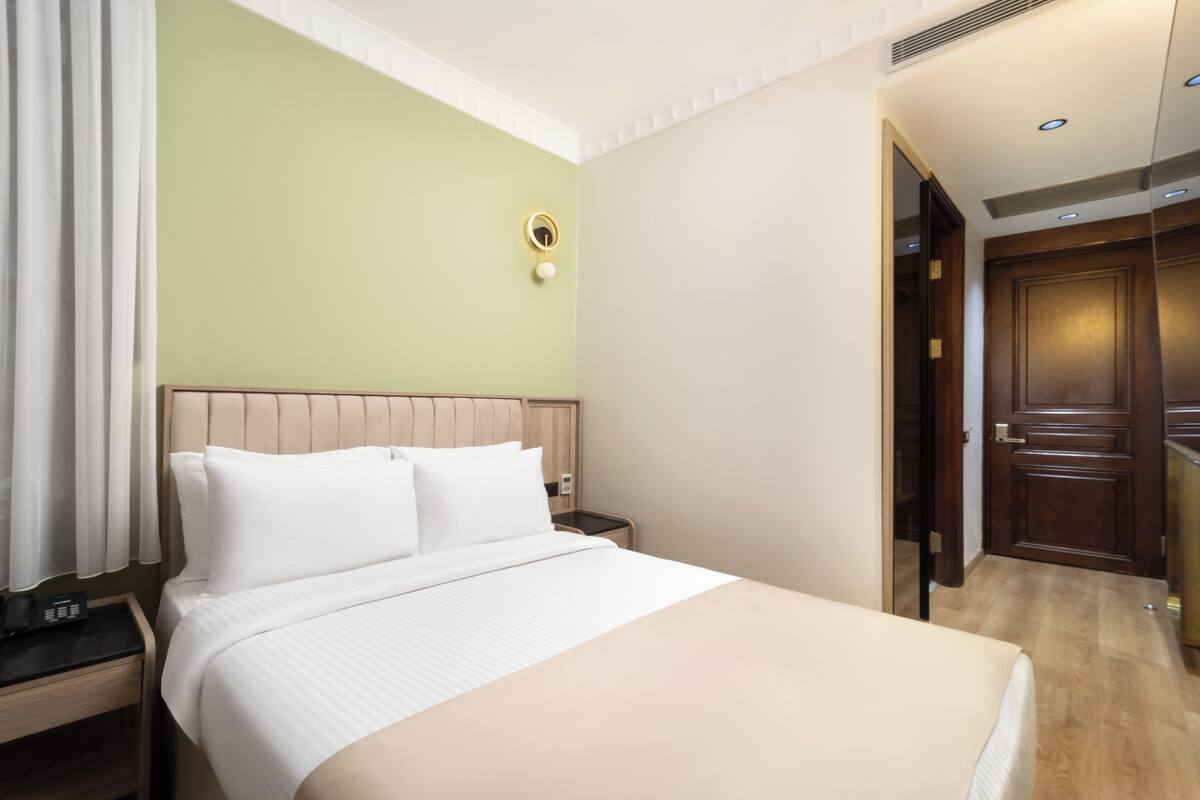 A hotel room with a bed, bedside table, and a mirror.