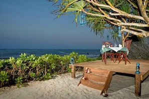 A wooden deck with a table and chairs, overlooking the beach and ocean.