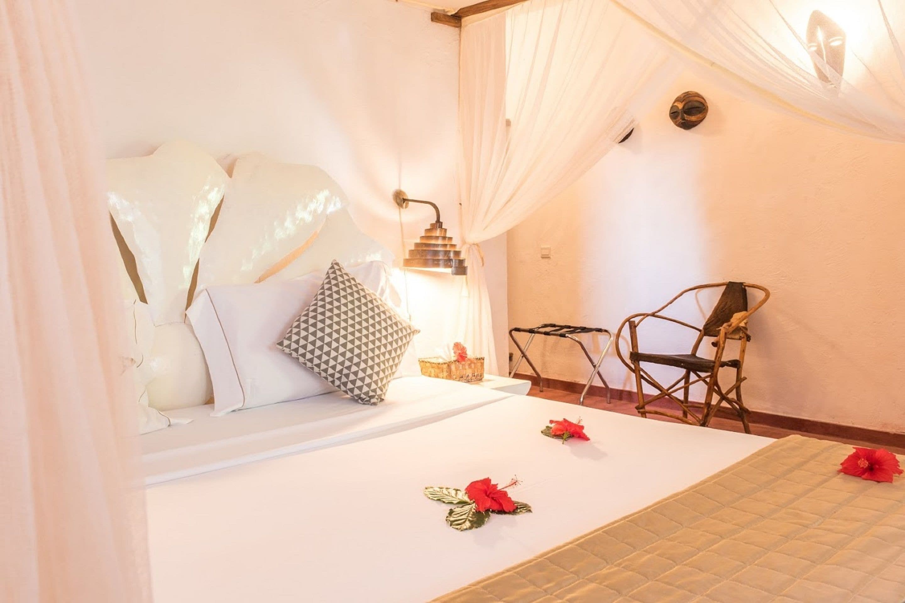 A bedroom with a bed, pillows, a chair, a small table, and a decorative mask on the wall.