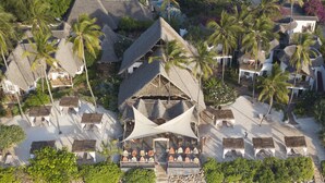 Un complexe hôtelier de bord de mer avec des bâtiments aux toits de chaume, des palmiers et des parasols de plage.