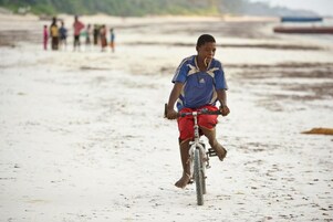 Una persona anda en bicicleta sobre una playa arenosa, con un grupo de personas al fondo.