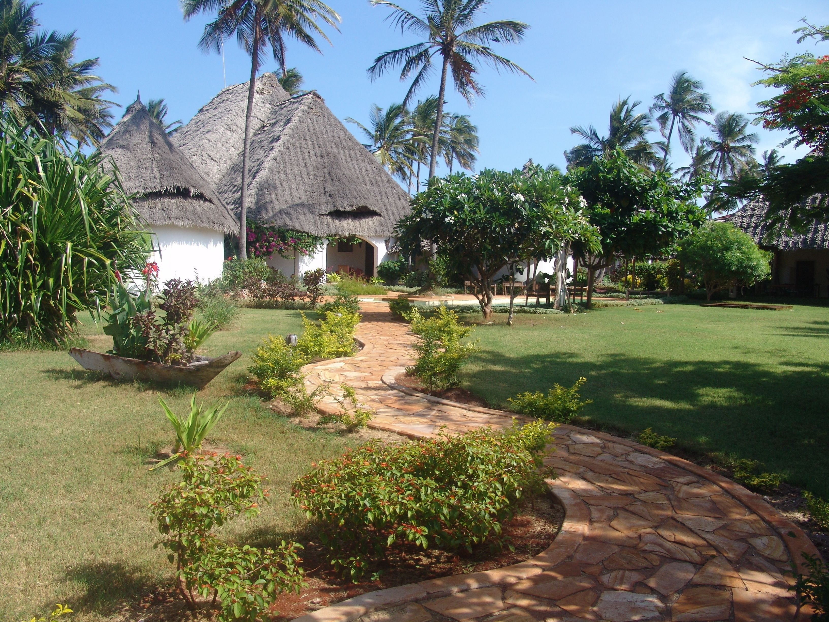 A tropical resort with thatched-roof huts, a stone pathway, and lush greenery.
