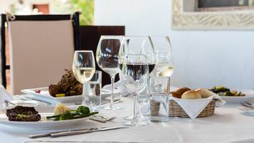 A dining table set with plates of food, wine glasses, and a basket of bread.