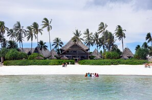 A beachside resort with thatched-roof buildings, palm trees, and a sandy beach.