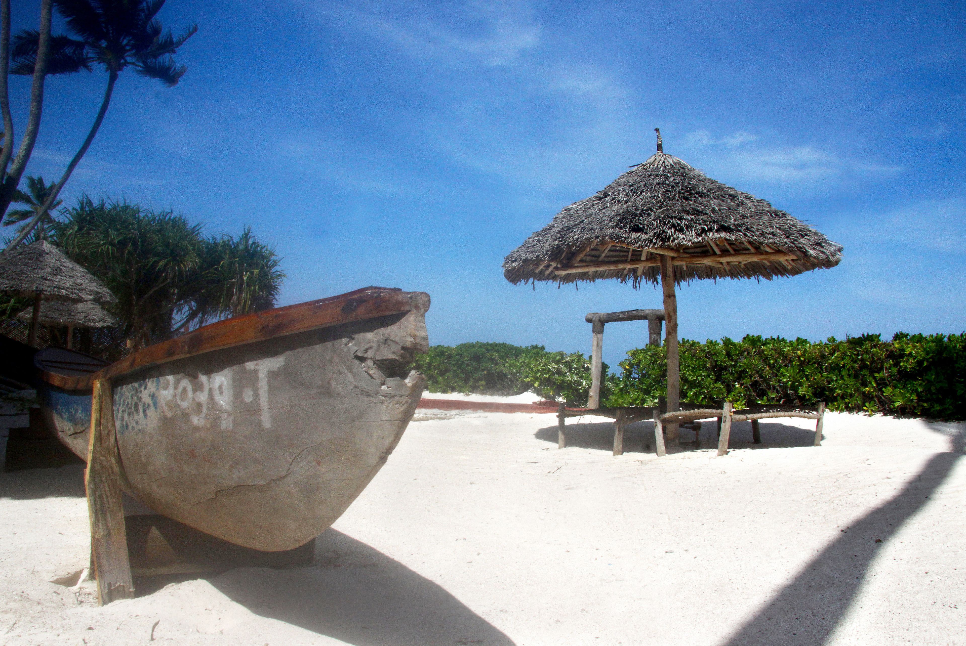 A boat on a sandy beach with a thatched-roof structure nearby.