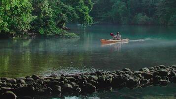 A person in a canoe on a calm river surrounded by rocks and dense greenery.