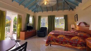 A hotel room with a bed, a desk, a chair, a TV, and a ceiling fan. - Tropical Lagoon Resort (Port Antonio)
