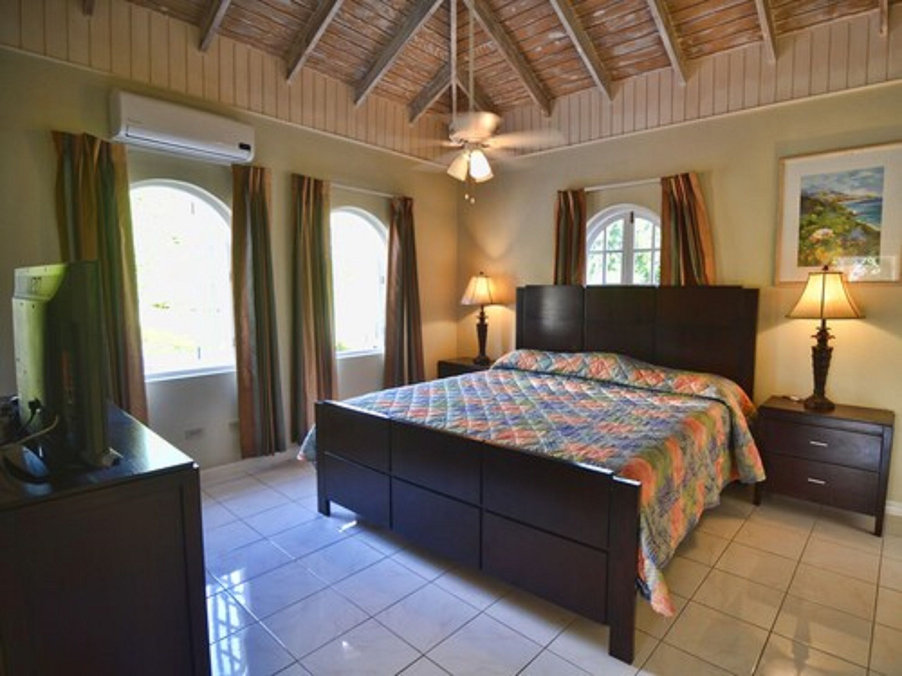 A bedroom with a bed, two bedside tables, a ceiling fan, and windows with curtains.