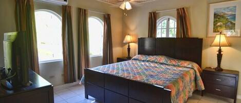 A bedroom with a bed, two bedside tables, a ceiling fan, and windows with curtains.